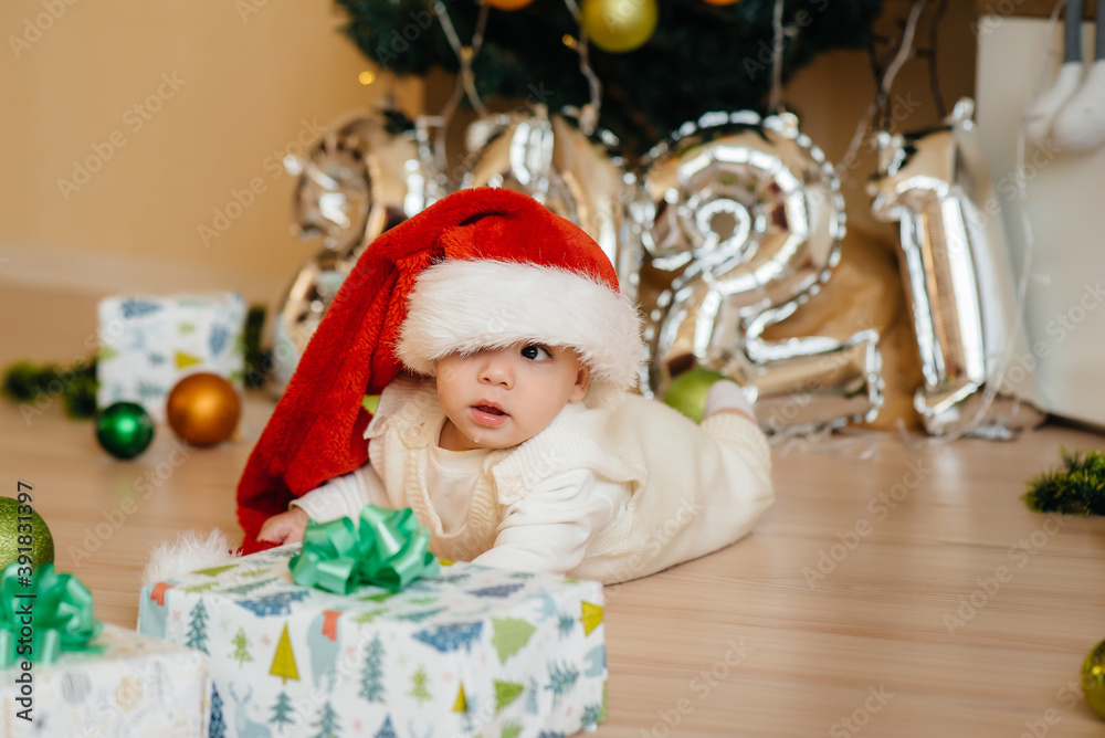 Cute smiling baby is lying under a festive Christmas tree and playing with gifts. Christmas and New Year celebrations Cute smiling baby is lying under a festive Christmas tree and playing with gifts. Christmas and New Year celebrations