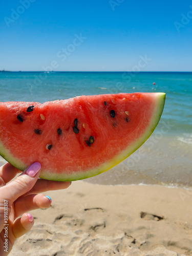 watermelon slice in hand against the sea and sky background. close-up