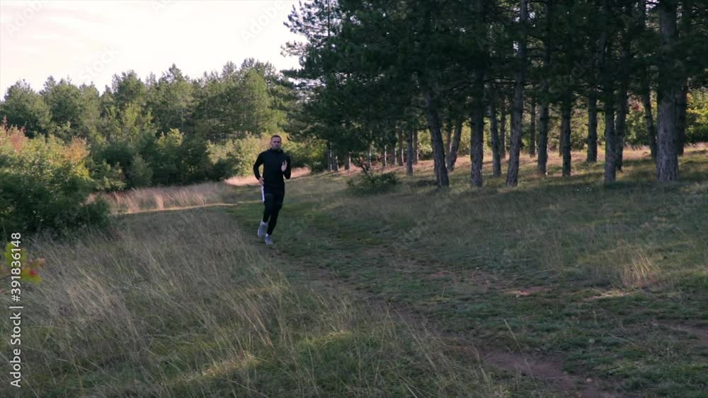 Man running on a forest path. Athlete jogging in woods with evergreen trees. Man running on a forest path. Athlete jogging in woods with evergreen trees.
