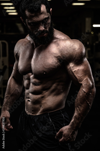 strong sport athlete male with beard and perfect physique body in dark fitness gym