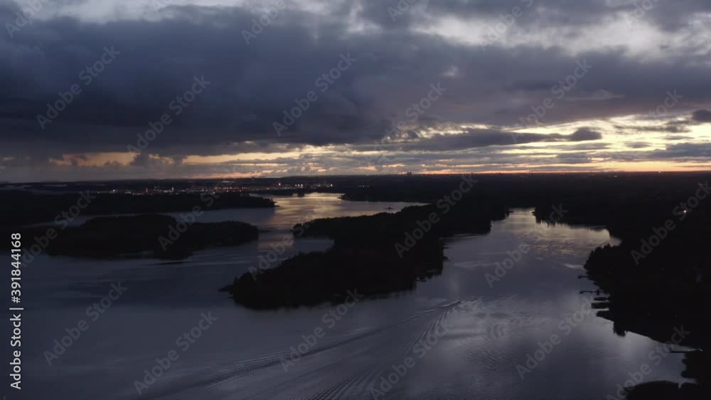 Boat sails between islands in the sea with city lights on the horizon. Track right. Boat sails between islands in the sea with city lights on the horizon. Track right.