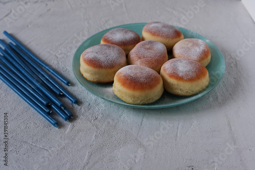 Jewish holiday Hanukkah concept. Blue candles and traditional Hanukkah food doughnuts with sugar powder (sufganiyot) on a grey concrete background.