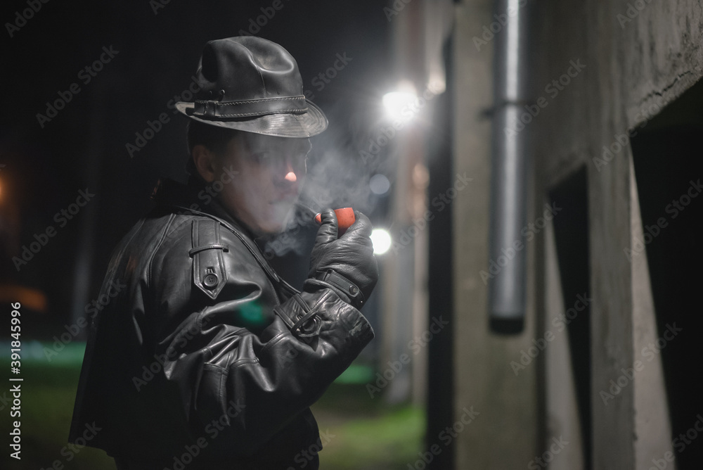 Detective agent in black leather hat and coat smokes a smoking pipe.