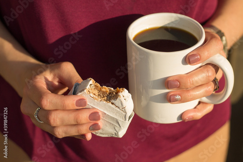 Woman hands holding breakfast coffee and alfajor with cream dulce de leche and powdered sugar. Selective focus and blur background on sunny day.