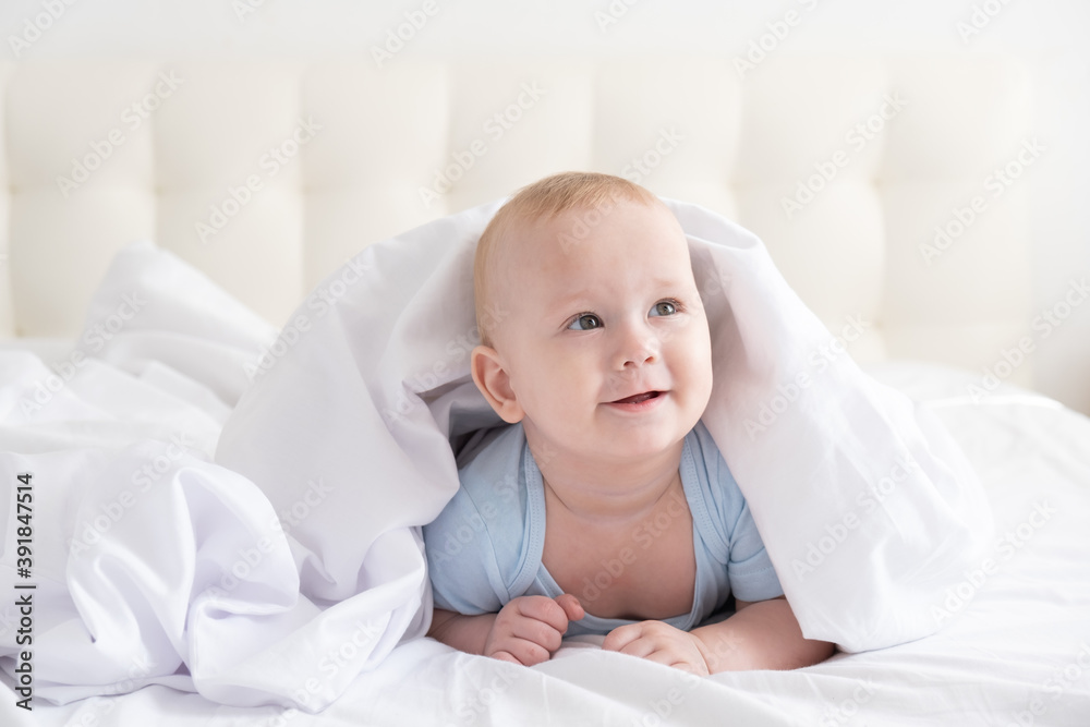 funny baby boy smiling and lying on a white bedding at home. 