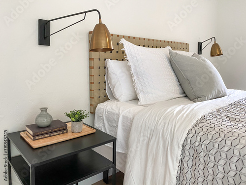 Bed maid-up with clean white and gray pillows and bed sheets in bedroom with small side table and lamp photo