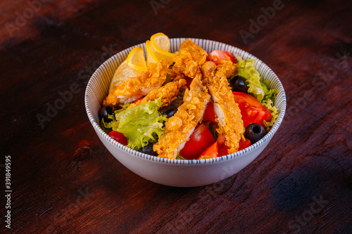Healthy salad with fillet chicken, tomatoes, lettuce, olives, lemon and sauce in bowl on wooden background. Healthy food, clean eating, dieting, top view