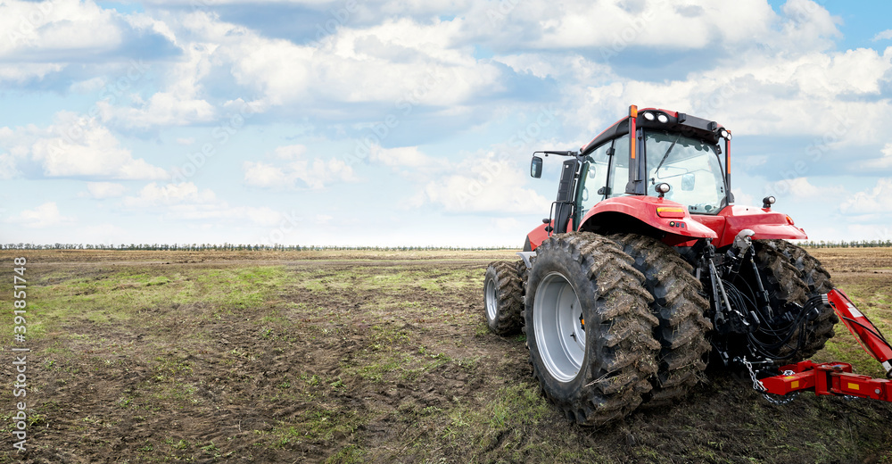 Fototapeta premium Modern tractor cultivates fertile land under a cloudy sky