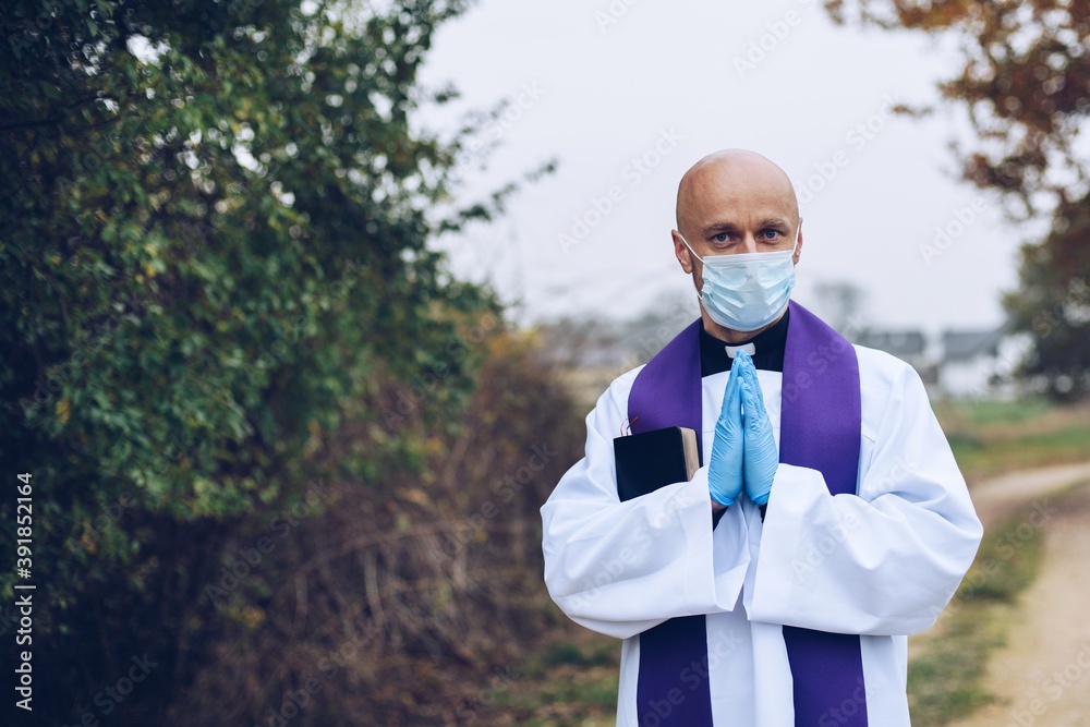 Praying priest in a protective mask and protective gloves somewhere on the road Praying priest in a protective mask and protective gloves somewhere on the road