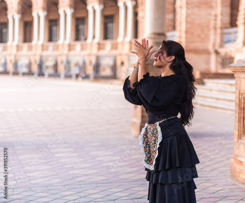 Stock photo of a flamenco dancer in a black dress in a square. Woman clapping and dancing flamenco outdoors.