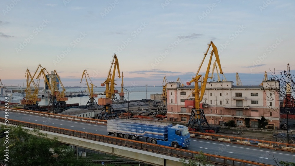 Industrial port landscape with cargo cranes and cargo vehicle traffic by overpass Industrial port landscape with cargo cranes and cargo vehicle traffic by overpass