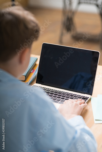 Young student watching lesson online and studying from home. Young boy taking notes while looking at computer screen on video call. Girl studying from home on pc.