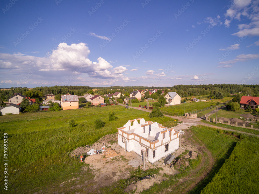 Aerial view on detached house under construction. House in basic state. Located on green plot in small village. Lack of wooden roof structure. Meadows 