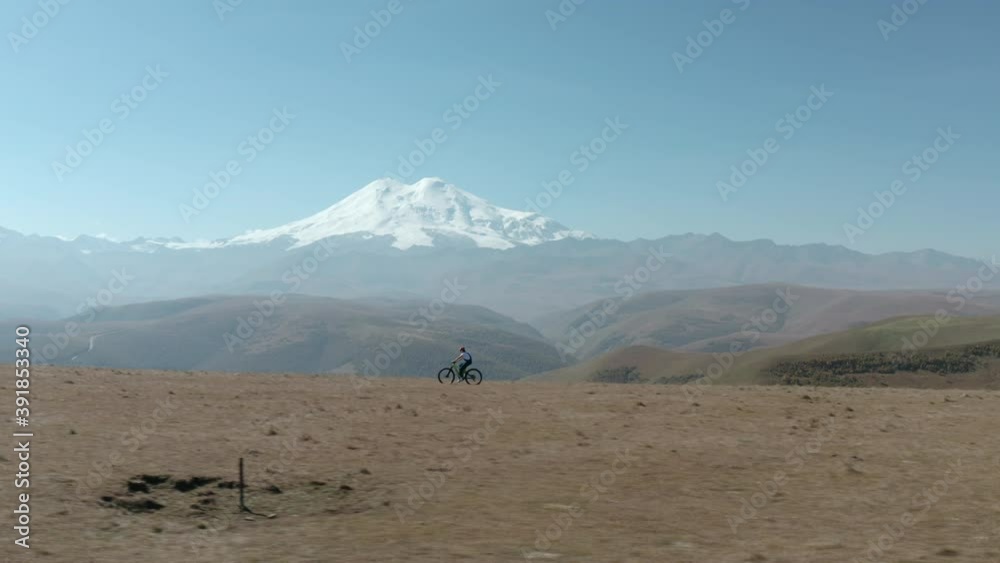Bicycle woman riding bike on snowy mountain peak background. Tourist girl traveling on sport enduro full suspension e-bike bicycle on mountain plain on snowy Elbrus landscape. Bicycle woman riding bike on snowy mountain peak background. Tourist girl traveling on sport enduro full suspension e-bike bicycle on mountain plain on snowy Elbrus landscape.