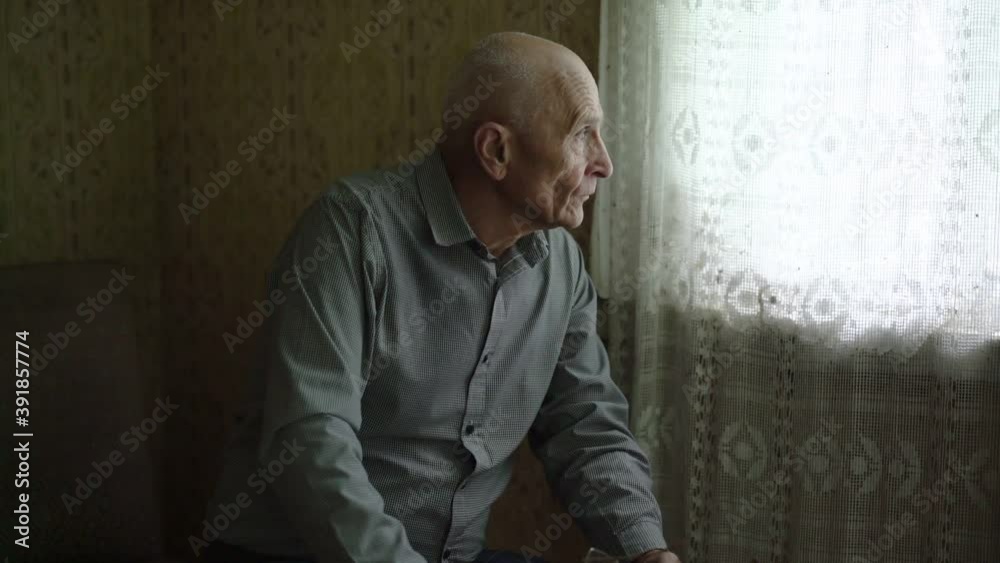 old bald lonely man sitting near window with white curtain at village house on quarantine indoor