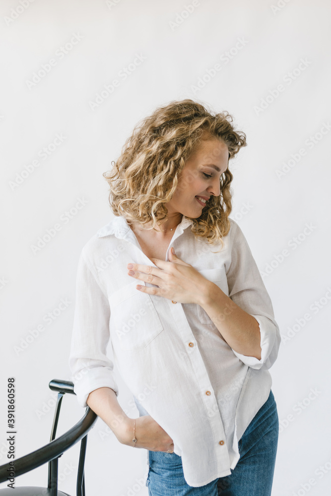Beautiful blonde girl in white shirt and jeans sitting on a chair on a white background in the studio. Beautiful blonde girl in white shirt and jeans sitting on a chair on a white background in the studio.