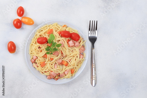 Italian spaghetti pasta with cherry tomatoes, tomato sauce, fried carrots and sausage on a light table, top view, place for text,, selective focus