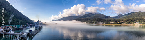 Panoramic shot of port of Juneau and mountains covered with clouds and fog in Gastineau Channel, Alaska. Cruise ship and boats docked in the port. Blue cloudy sky as a background