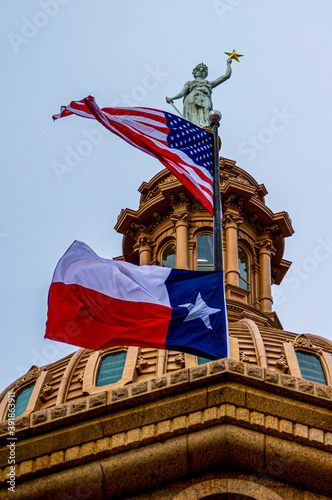 American and Texas State flag flying in front of the dome of the state house capital building in Austin.