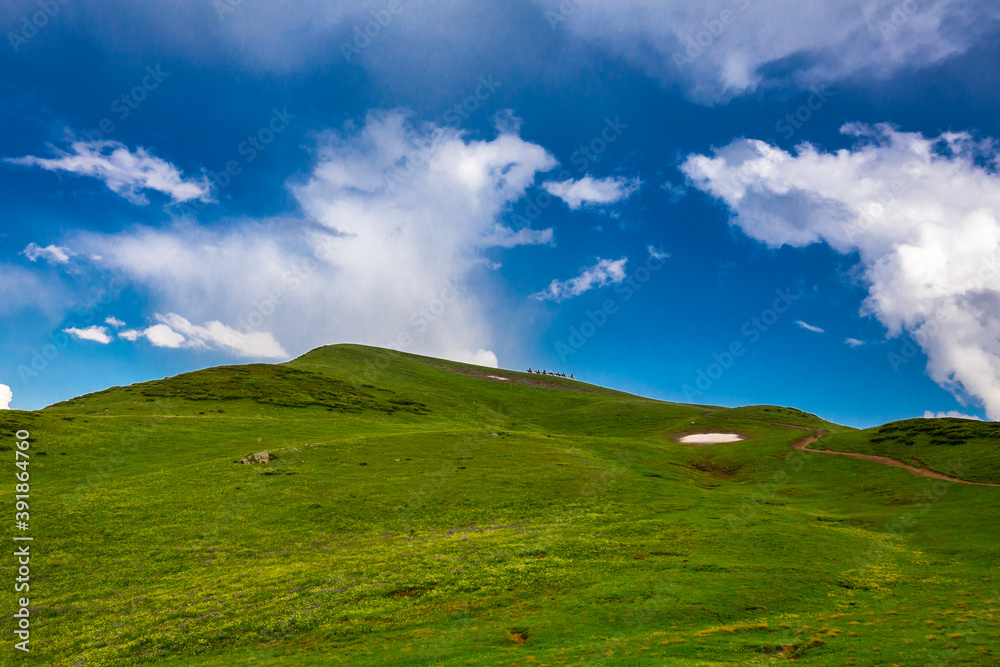 Beautiful mountain landscape at Caucasus mountains with clouds, blue sky and line of horse riders far away Beautiful mountain landscape at Caucasus mountains with clouds, blue sky and line of horse riders far away