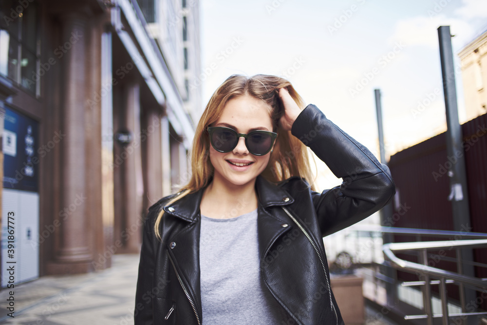 Fototapeta premium Happy woman model in a leather jacket walks down the street