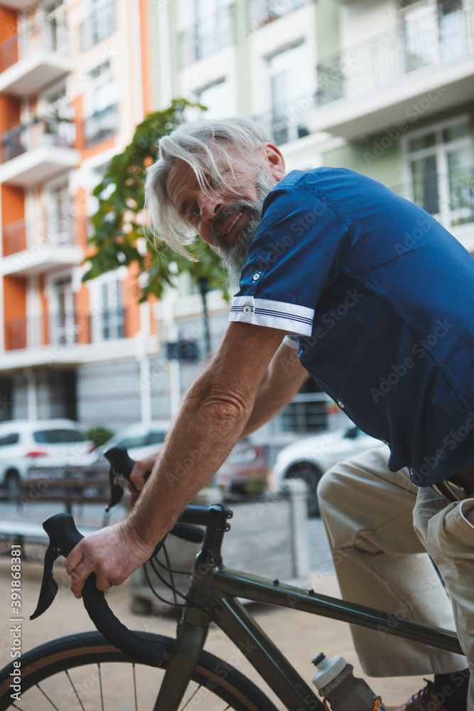 Obraz premium Vertical cropped portrait of a senior stylish bearded man cycling in the city