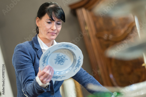 фотографія woman inspecting underside of antique plate to identify it