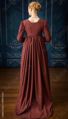 A Regency woman wearing a white dress, bonnet, and spencer standing alone in a room