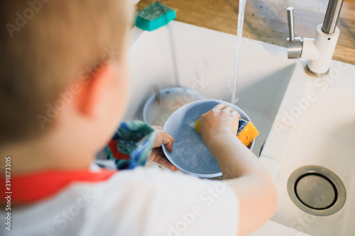 a little boy washes dishes in a modern kitchen.