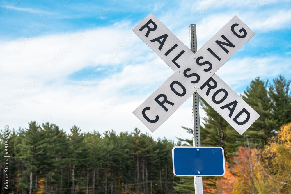 Obraz premium Railroad crossing sign with trees in background on aclear autumn day. Copy space.