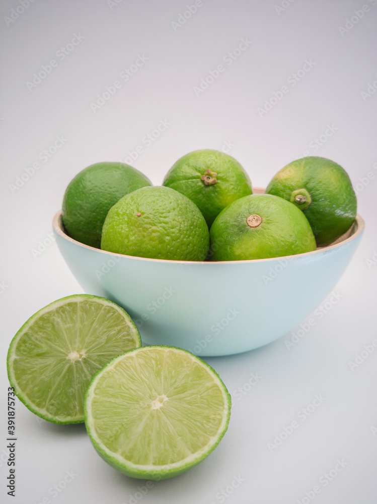 Light blue bowl with green limes and one lime outside cut in half on white background. Juicy colorful fruits for mojito. Freshness and health. Light blue bowl with green limes and one lime outside cut in half on white background. Juicy colorful fruits for mojito. Freshness and health.
