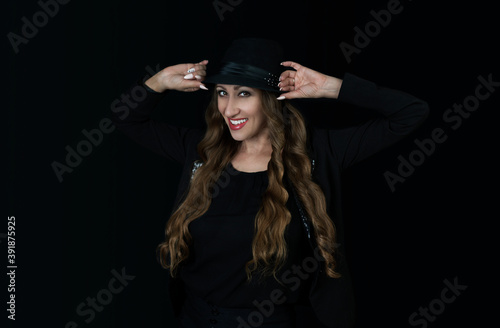 Woman in black hat on black background smiling. 