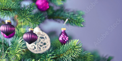 Banner with beautiful purple glass tree bauble with decorated Christmas tree with other seasonal tree ornaments on light violet background