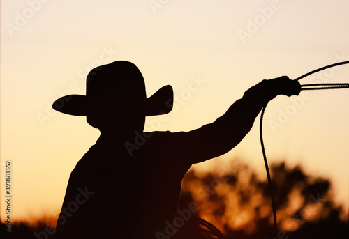 Young cowboy silhouette with sunset background, practice roping for rodeo industry.