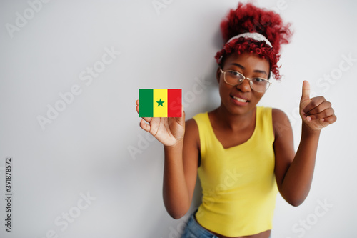 African woman with afro hair, wear yellow singlet and eyeglasses, hold Senegal flag isolated on white background, show thumb up. photo