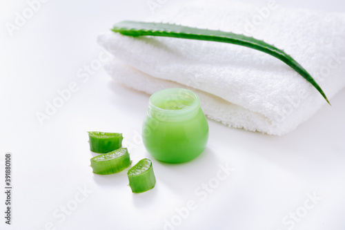 Organic cream with aloe slices and white towel on background