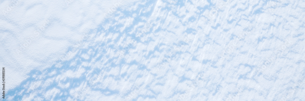 Beautiful winter background with snowy ground. Natural snow texture. Wind sculpted patterns on snow surface. Wide panoramic texture for background and design.