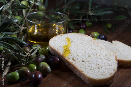Olive oil in a glass vase with olive branches and olives around on a wooden table