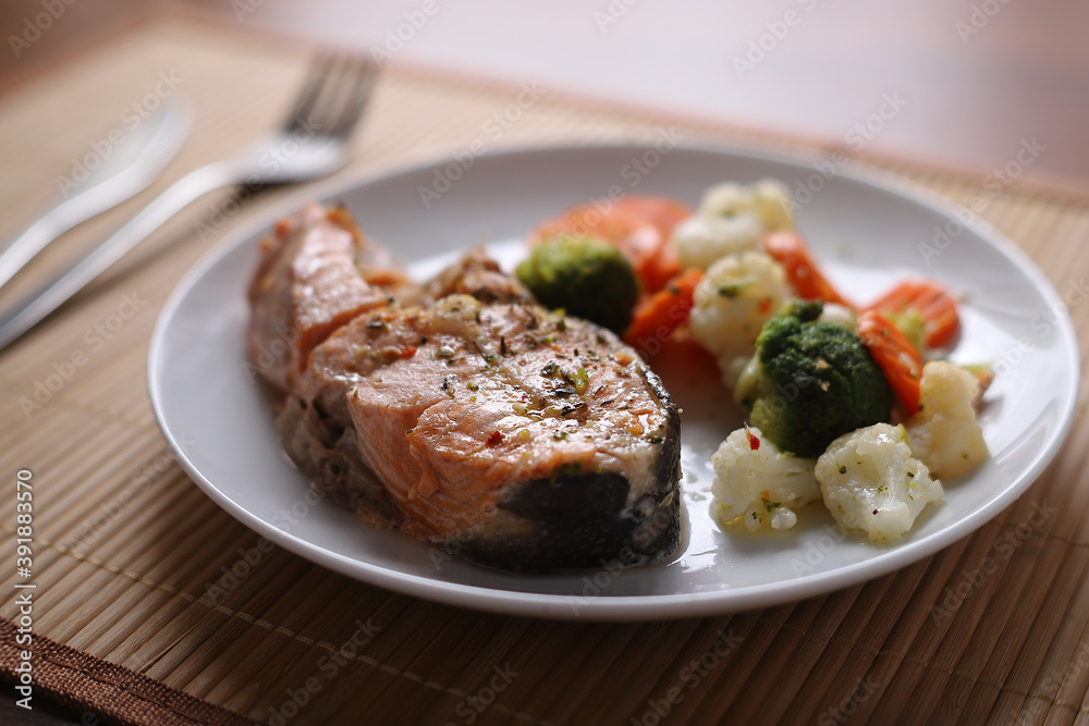 Baked salmon with steamed vegetables on a white plate close-up