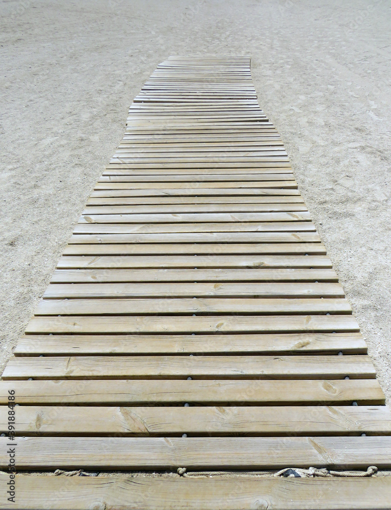 Wooden footbridge in the sand of a beach for access to the sea. Perspective view of beach trotter. Articulated wooden walkway background. Littoral equipment concept.