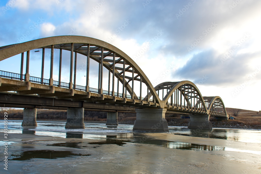 An arched steel and concrete bridge spanning a partially frozen river along the trans-Canada highway in Saskatchewan, Canada.