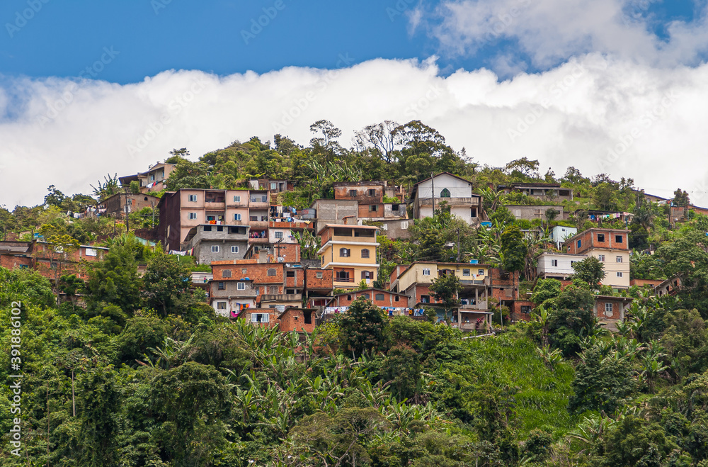 Petropolis, Brazil - December 23, 2008: Group of multi-story, red brick cheap housing set on green tropial forested hill under blue cloudscape. Laundry adds color.