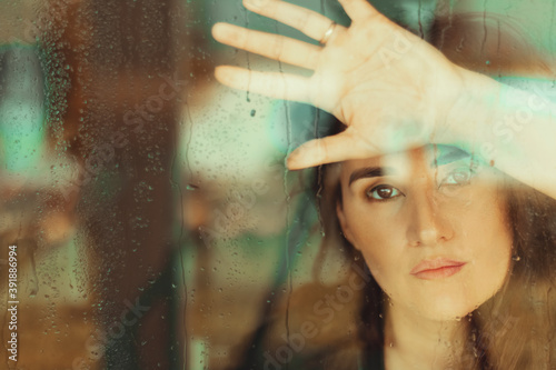 Mulher por trás de um vidro, encarando a câmera, com olhar de tristeza photo