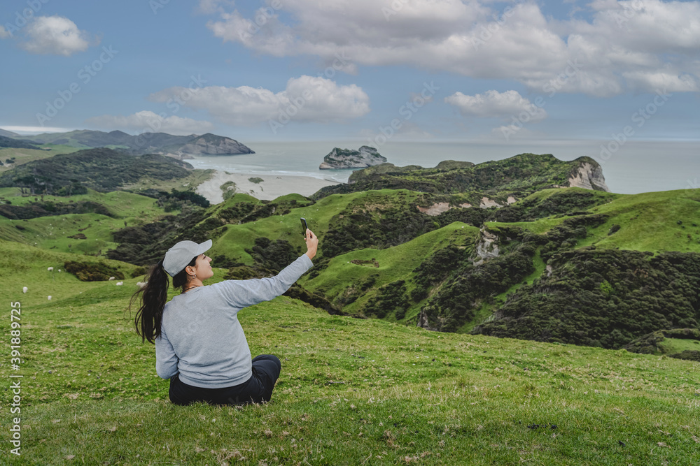 Young woman sitting on hillside on Wharariki beach view point. New Zealand