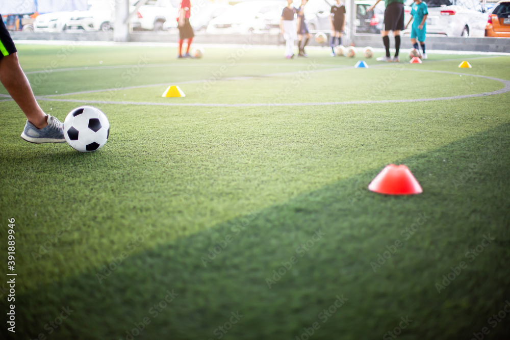 Obraz premium Soccer player shoot ball with blurry kid soccer team training. Blurry kid soccer player jogging between marker cones and control ball with soccer equipment in football academy.