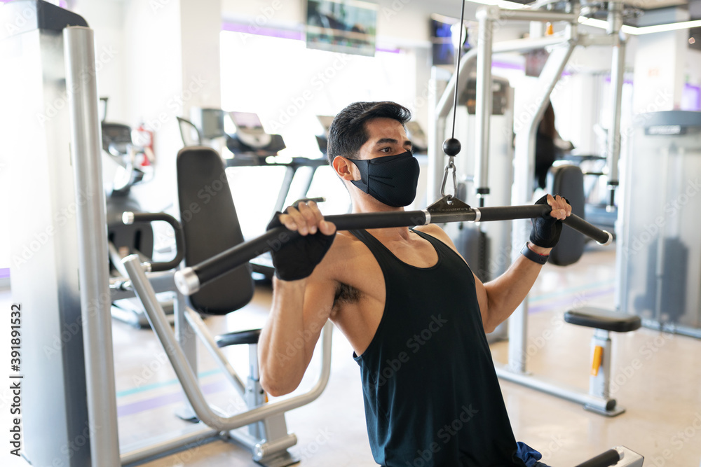 Fototapeta premium Young man with a mask exercising in the cable machine