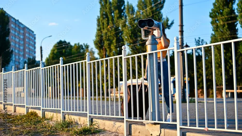 Young woman in protective medical mask looking into a tower viewer from the observation deck at the city at sunset. Corona Virus idea. Safe travel during the pandemic. Slow motion. Chisinau, Moldova