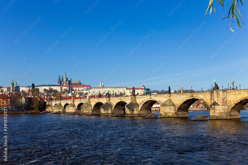 Obraz premium Autumn colorful Prague Lesser Town with gothic Castle and Charles Bridge above River Vltava in the sunny Day, Czech Republic