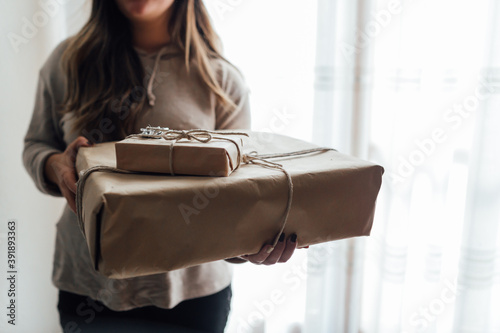 Young woman holds in hands stacked Christmas gift boxes in craft paper with juniper. Christmas presents concept.