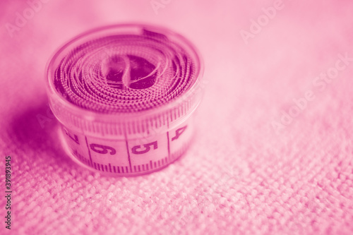 Measuring tape in box on the table. Pink tone.